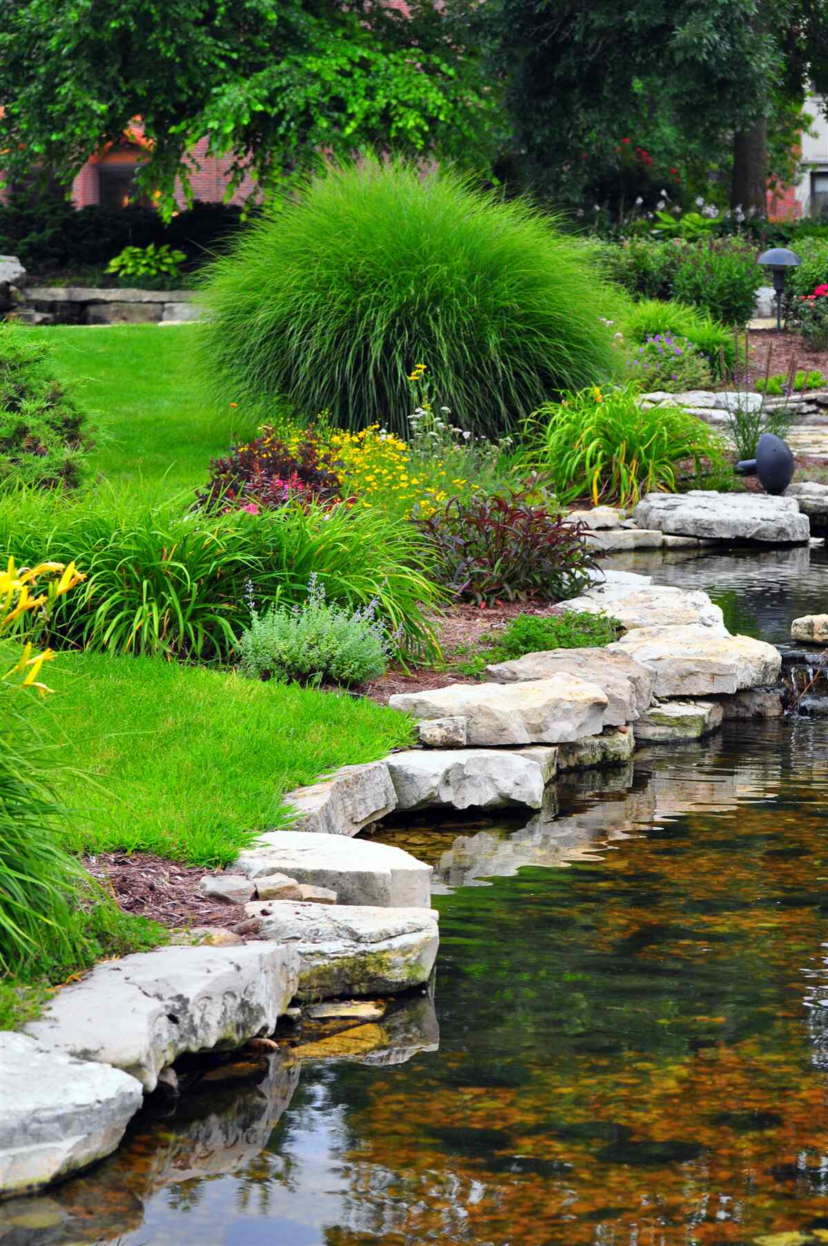 Fotobehang bloemen bij een vijver in de tuin